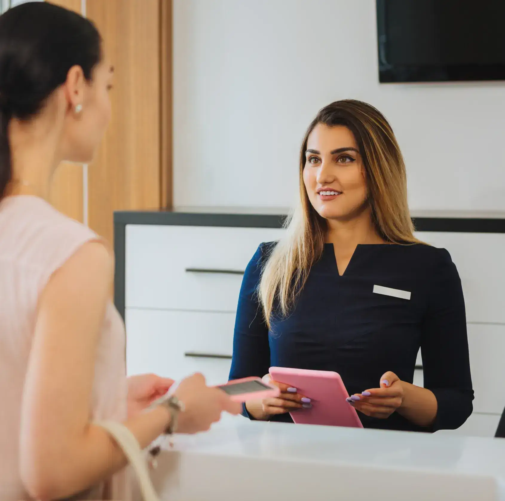 A friendly AsterSmiles receptionist greeting a patient at the front desk of a modern dental office.