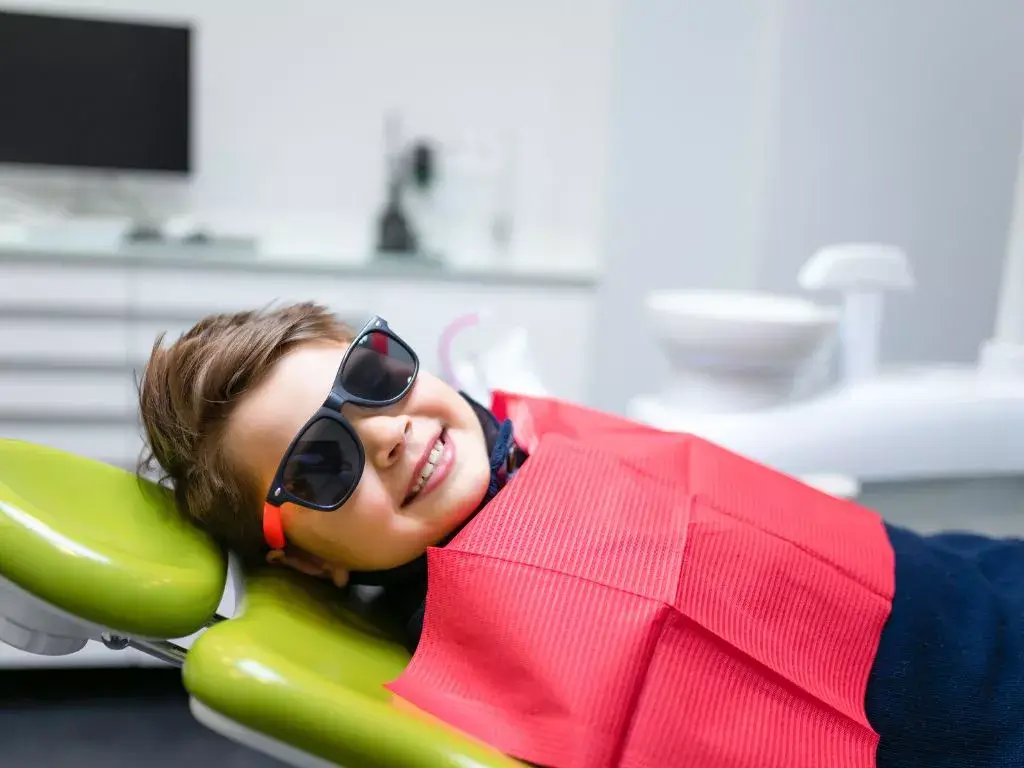 A happy young patient wearing sunglasses while relaxing in a dental chair, highlighting the comfortable and kid-friendly dental services available at AsterSmiles.